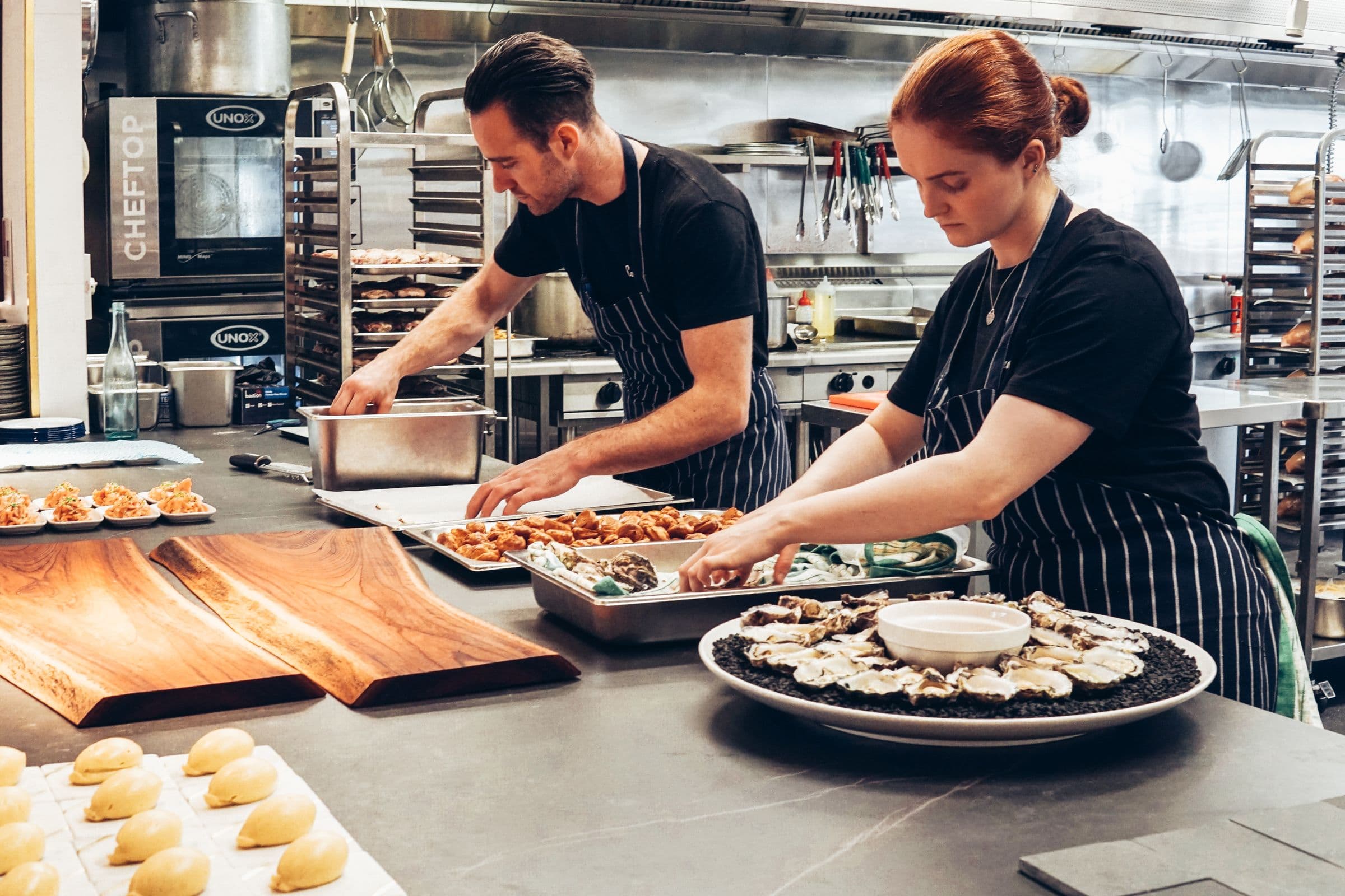Two cooks working a prep line with hotel pans